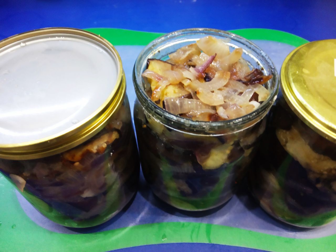 Закуска из баклажанов и лука, на зиму: В каждую банку добавляем перец, уксус накрываем пропаренными крышками и ставим в кастрюлю с горячей водой.