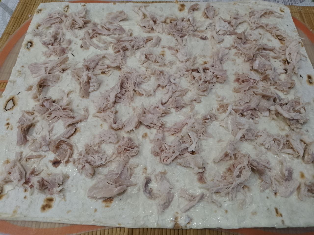 Вкусная закуска из лаваша, куриного филе и сыра, на сковороде: Распределяем равномерно куриное мясо, не до края с той стороны, где будем сворачивать рулетом.