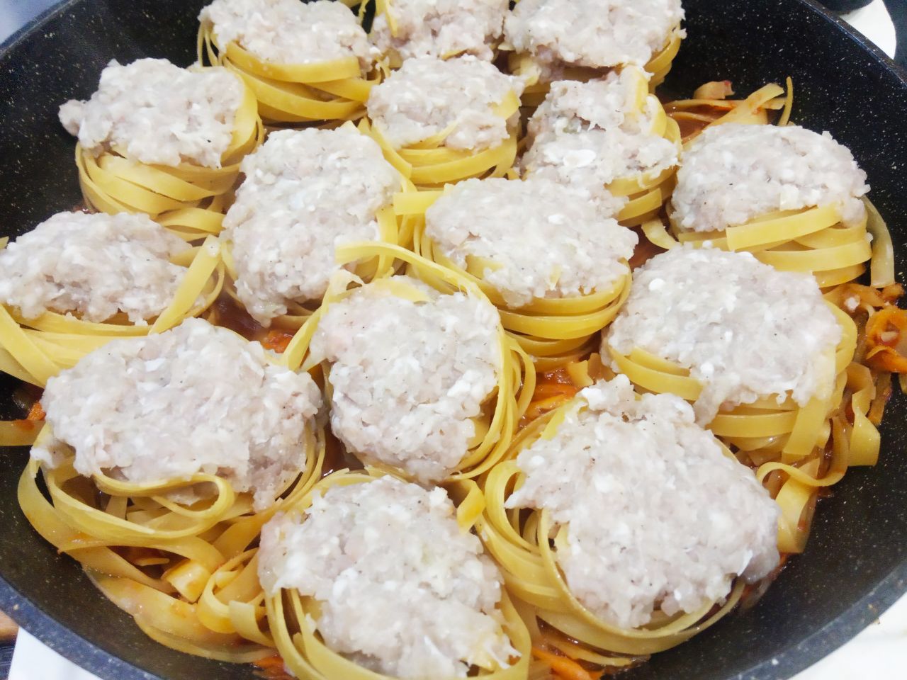 Макаронные гнёзда с фаршем и сыром на сковороде: Макаронные гнезда плотно наполняем начинкой и укладываем фаршированные гнёзда в сковороду. Доливаем водой