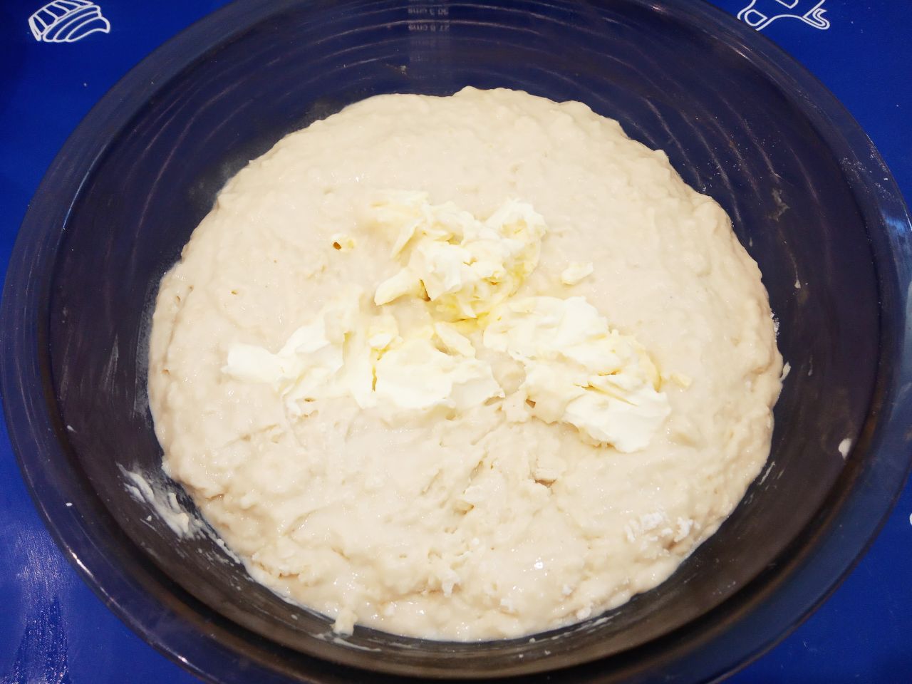 Воздушные и мягкие булочки с изюмом, в сахарной глазури: Сливочное масло разрезаем на кусочки и кладем в тесто, тщательно размешиваем.