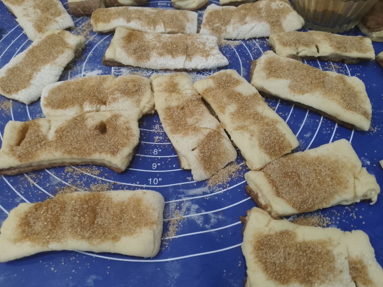 Булочки из слоеного теста с корицей и изюмом: Переворачиваем прямоугольники светлой стороной, посыпаем корицей с сахаром половину прямоугольников,