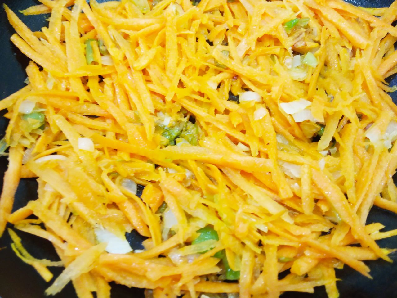 Острые чесночные стрелки жареные с луком и морковью: Добавляем к обжаренному луку тертую морковь и обжариваем несколько минут.
