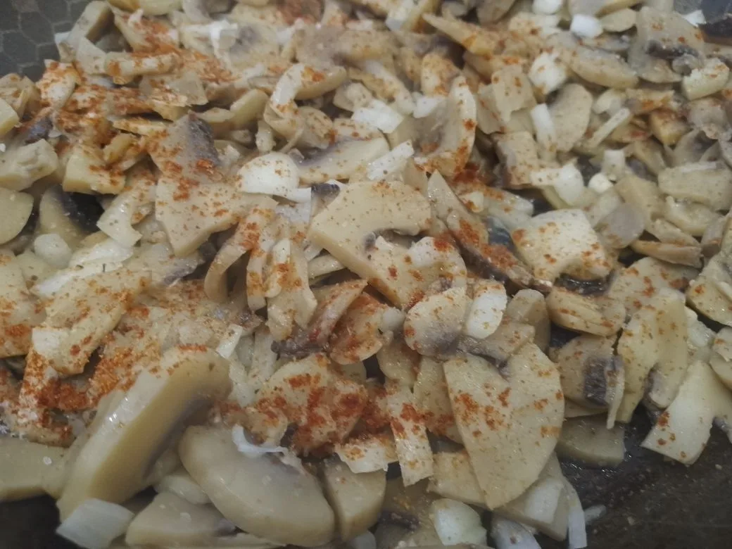 Картофель с начинкой из куриного мяса, шампиньонов и сыра: Добавляем растительное масло, измельченный лук, солим, перчим, посыпаем сушеным молотым чесноком и обжариваем