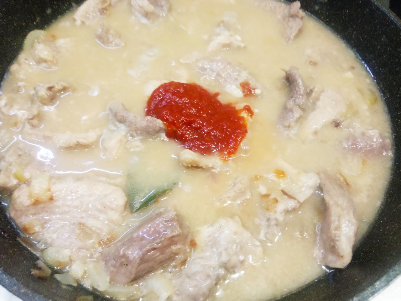 Мясо тушеное с луком и специями: Заливаем мясо с луком горячей водой полтора стакана, кладем томатную пасту, лавровый лист и размешиваем.