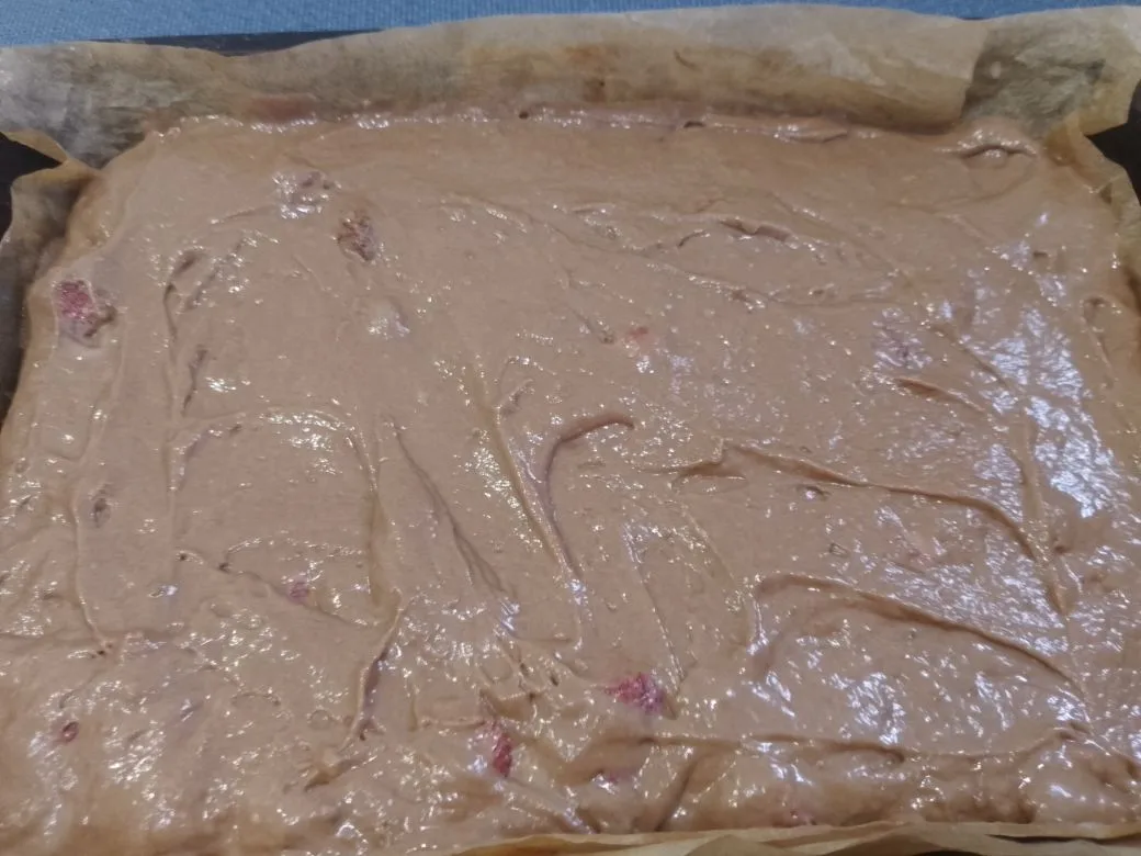 Шоколадный пирог на сметане, с клубникой и орехами: Форму размерами 30 х 20 застилаем пергаментом и выливаем тесто, разравниваем.