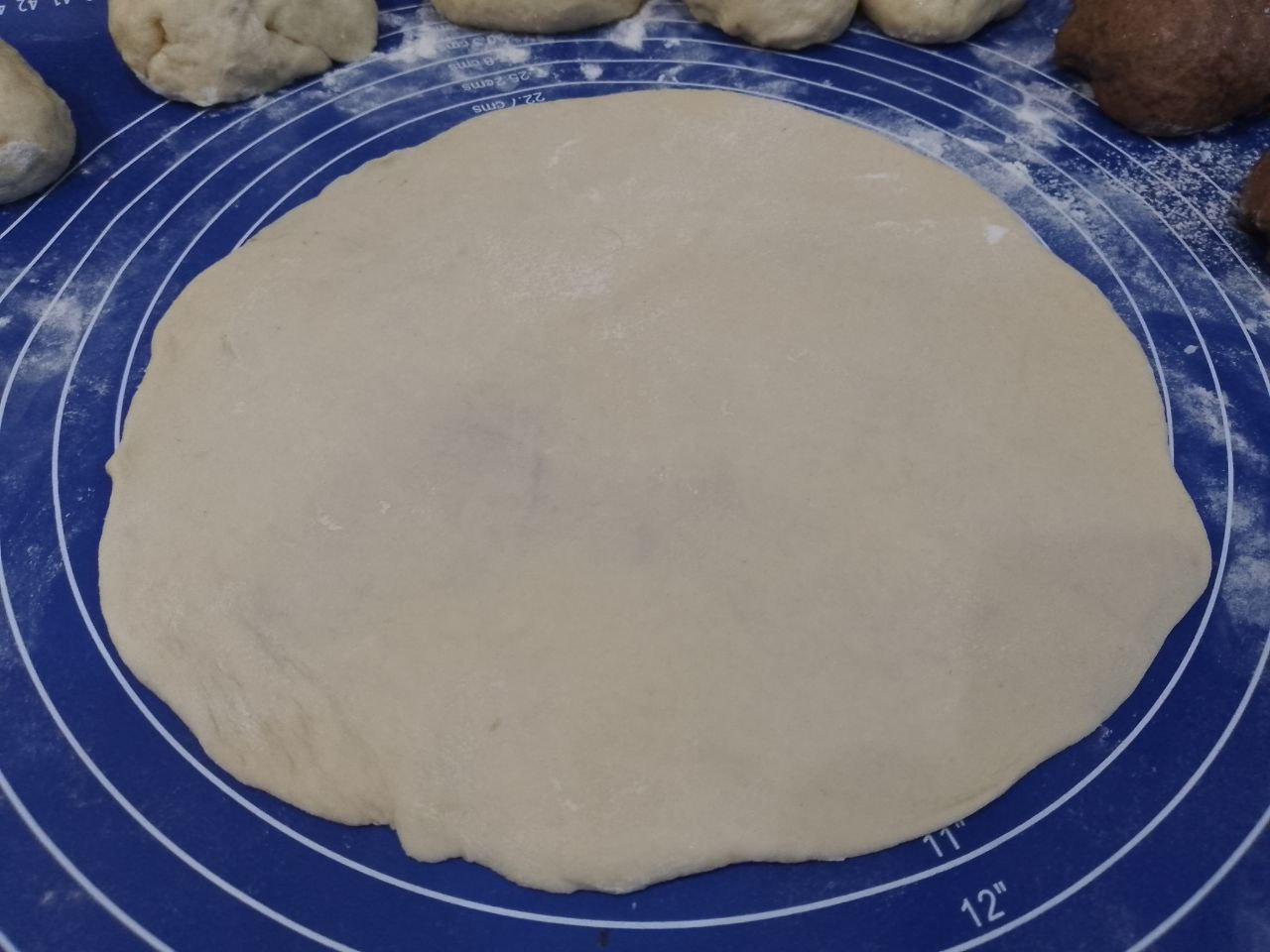 Булочки из слоеного теста с корицей и изюмом: Светлое тесто раскатываем формой круга и смазываем размягченным сливочным маслом.
