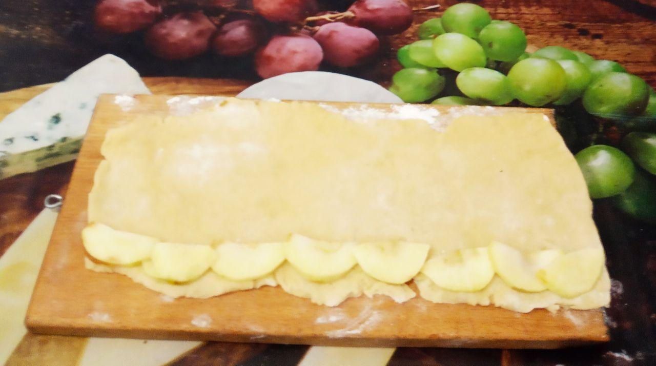 Печенье с творожной начинкой и яблоками: На длинную сторону листа на край выкладываем полоски яблок. Сворачиваем тесто рулетом и разрезаем на