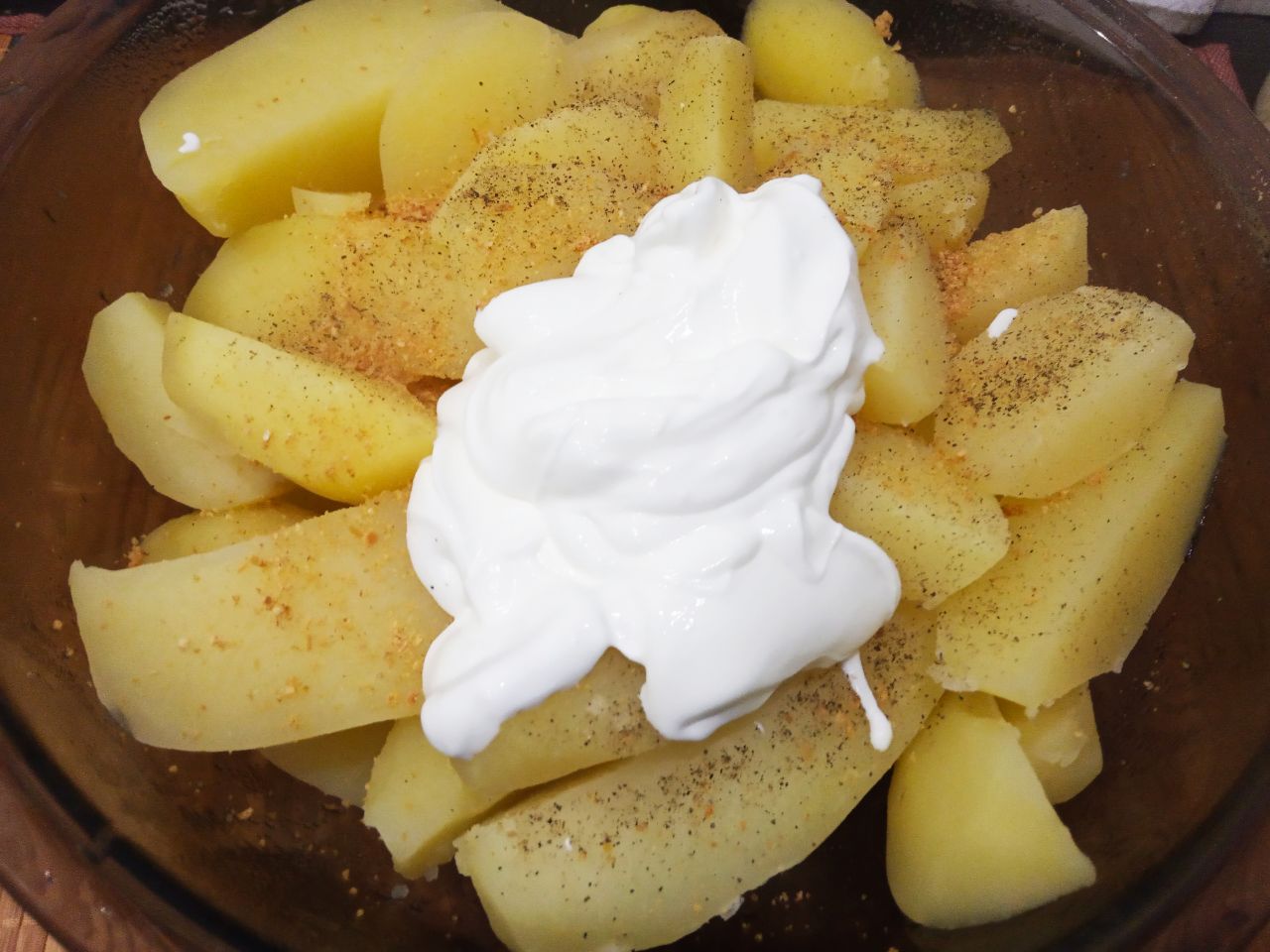 Запеченный молодой картофель в сметане и сыре: Складываем картофель в миску, добавляем перец молотый, сухой чеснок и сметану. Картофель перемешиваем