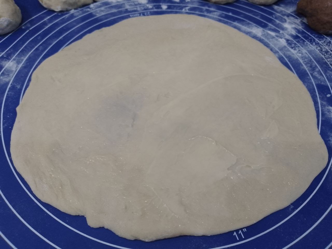 Булочки из слоеного теста с корицей и изюмом: Светлое тесто раскатываем формой круга и смазываем размягченным сливочным маслом.